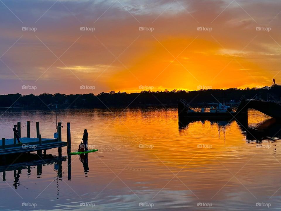 People taking an advantage of the nice weather by fishing and paddle boarding during a beautiful sunset