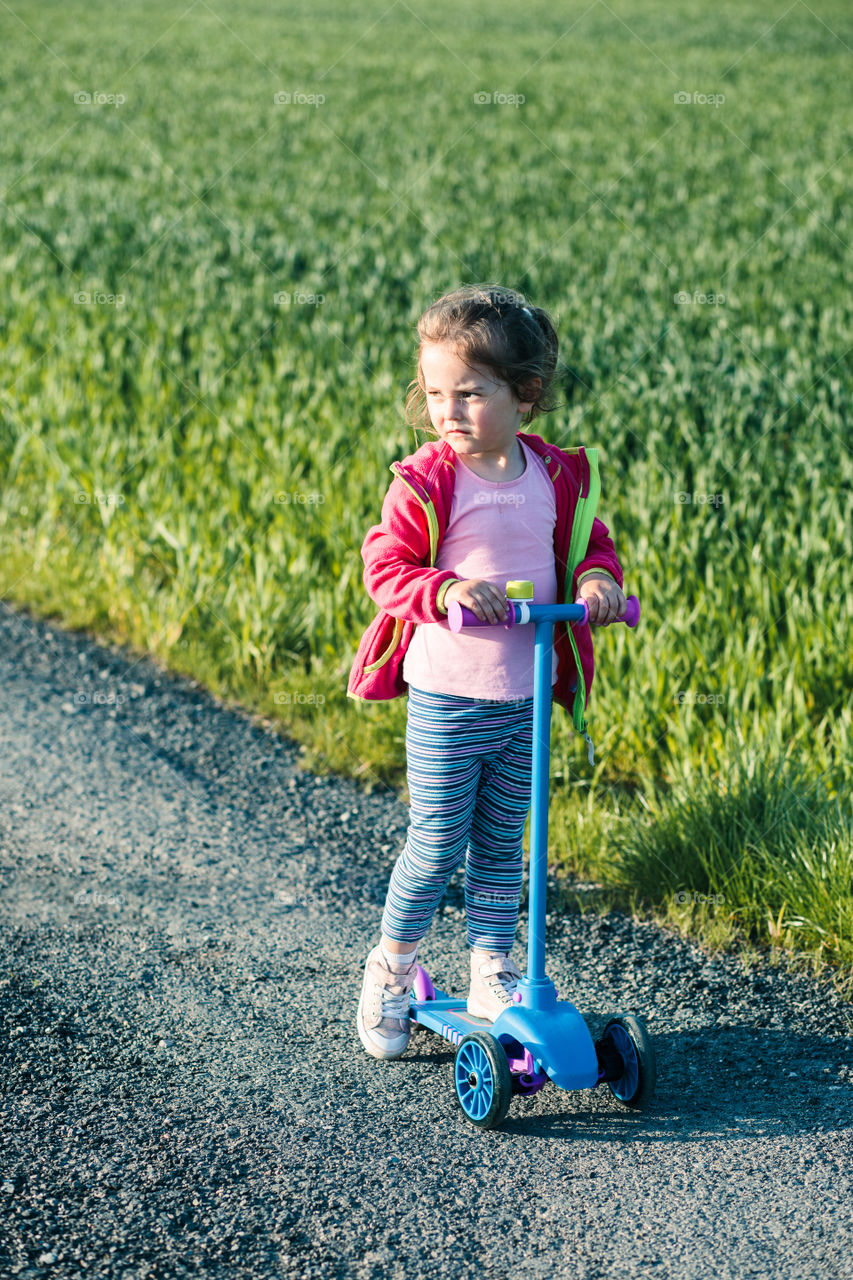 Little adorable girl having fun riding on scooter, playing outdoors. Real people, authentic situations