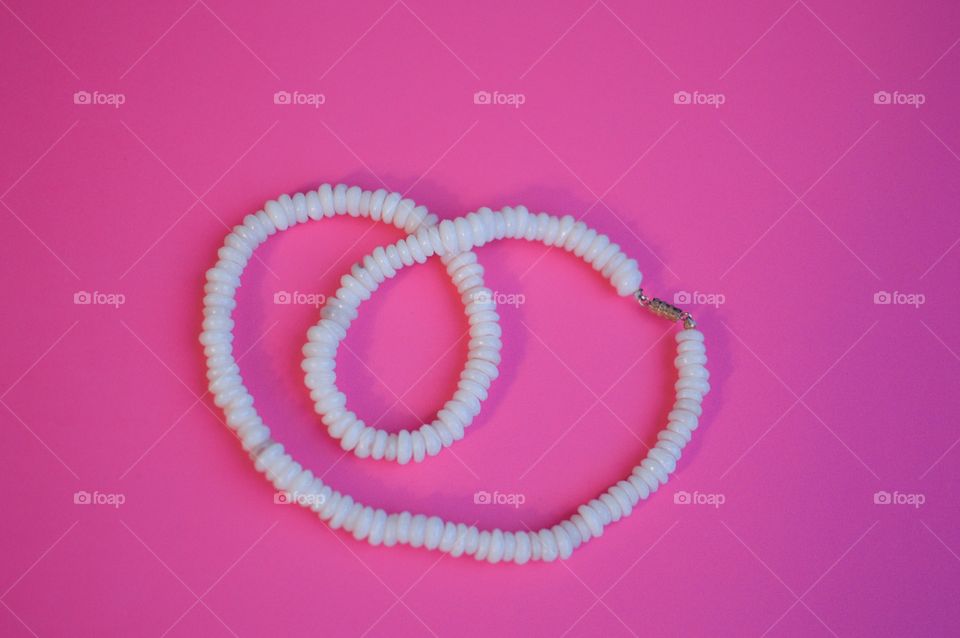 Contrasting flatlay on a bright pink background with a white shell necklace 