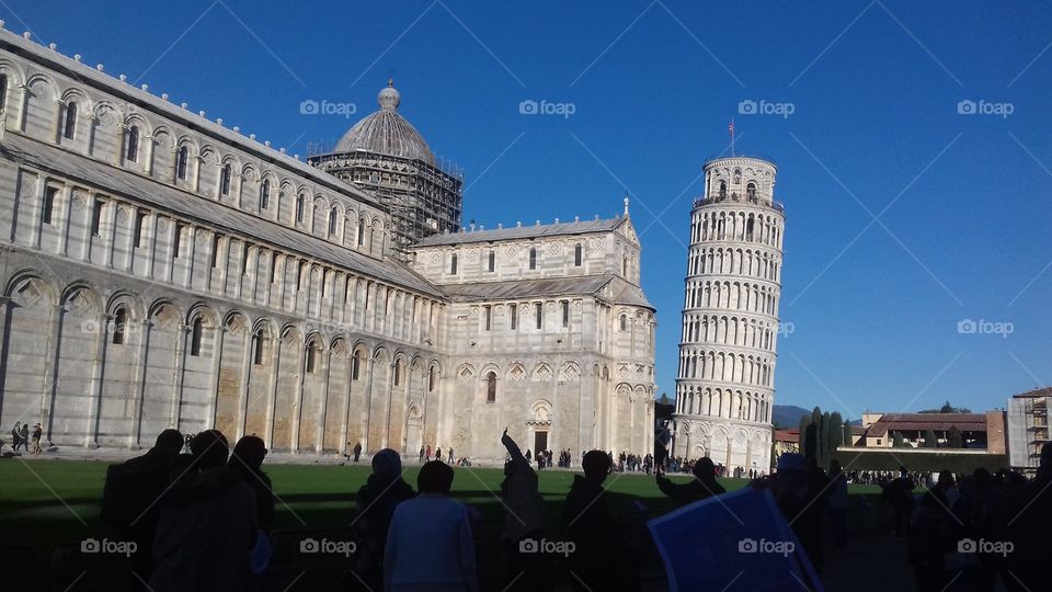 The tower of Pisa, one of the most important Italian monuments,framed from a distance with some people on a lawn to rest