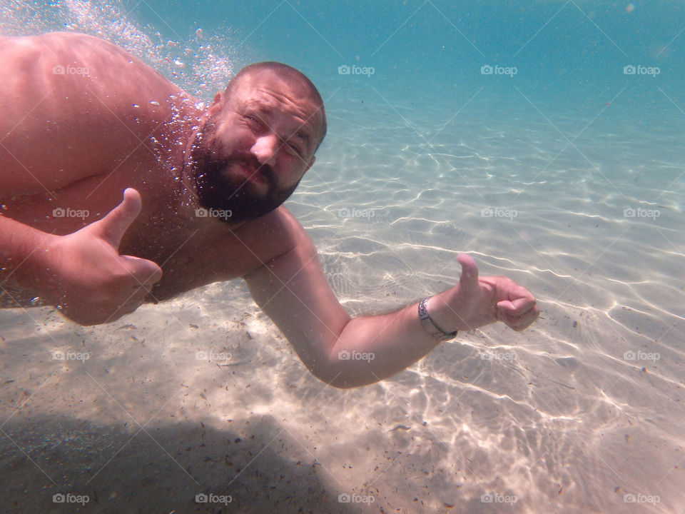 bearded man underwater. man with beard showing ok signs underwater