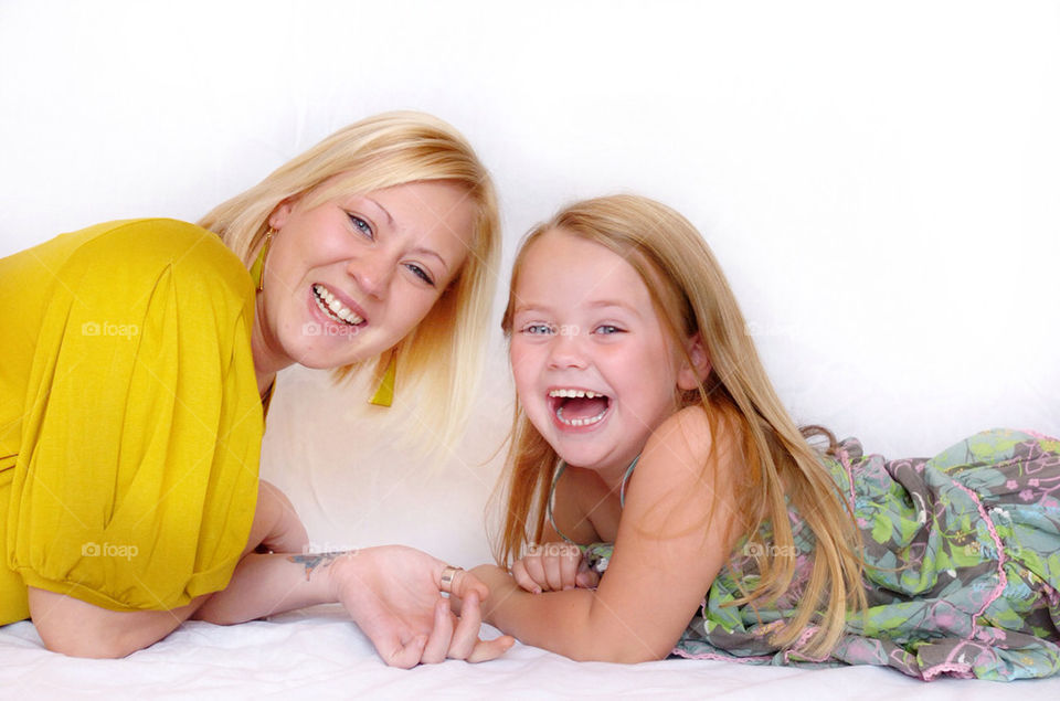 A YOUNG MOTHER AND HER DAUGHTER LAUGHING WHILE FACING THE CAMERA