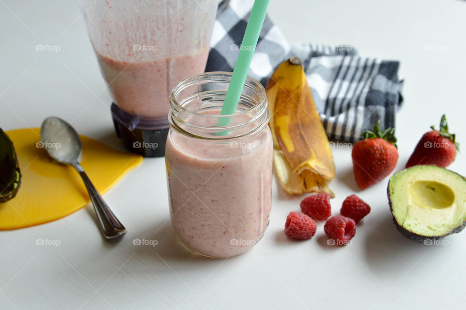 Smoothie and ingredients consisting of banana, raspberry, strawberry on a table
