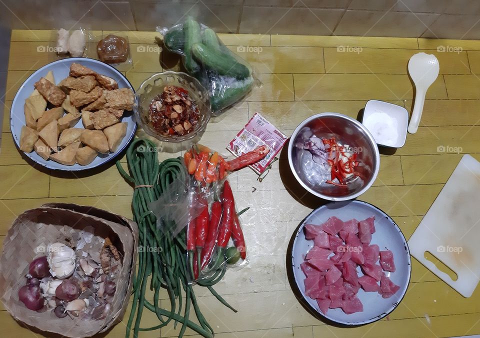 The various ingredients that is needed to cook some delicious food. These ingredients are garlics, onions, red meat, cucumber, carrot, tempeh, chillies, salt, and long beans.