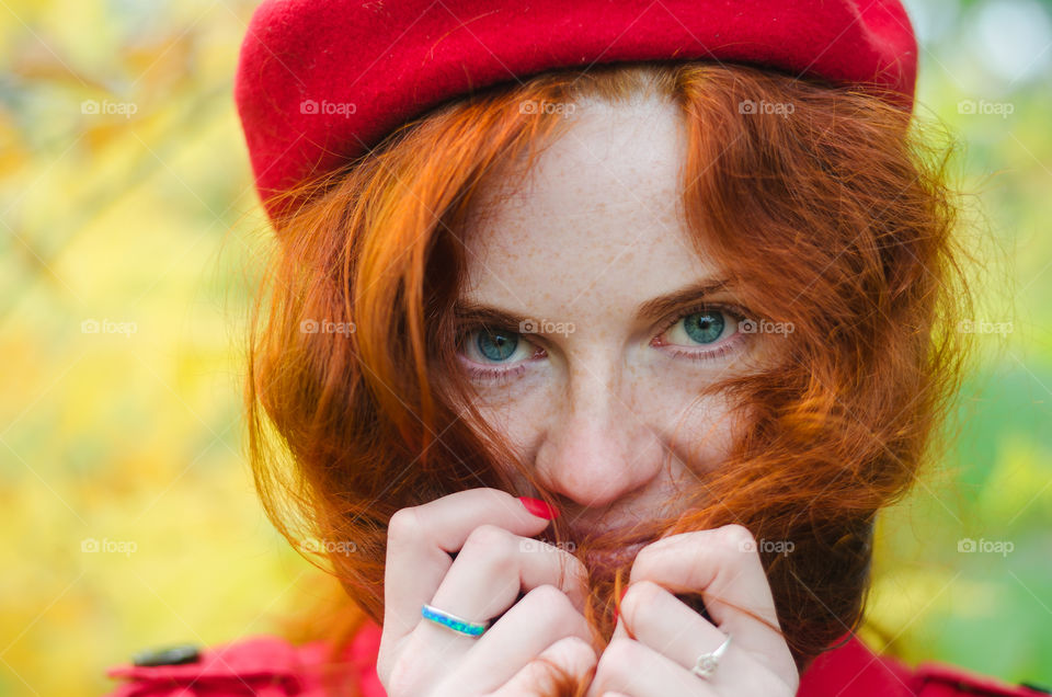 Portrait of a young redhead curly woman in red coat with freckles and blue eyes walking in autumn park. Happy people.