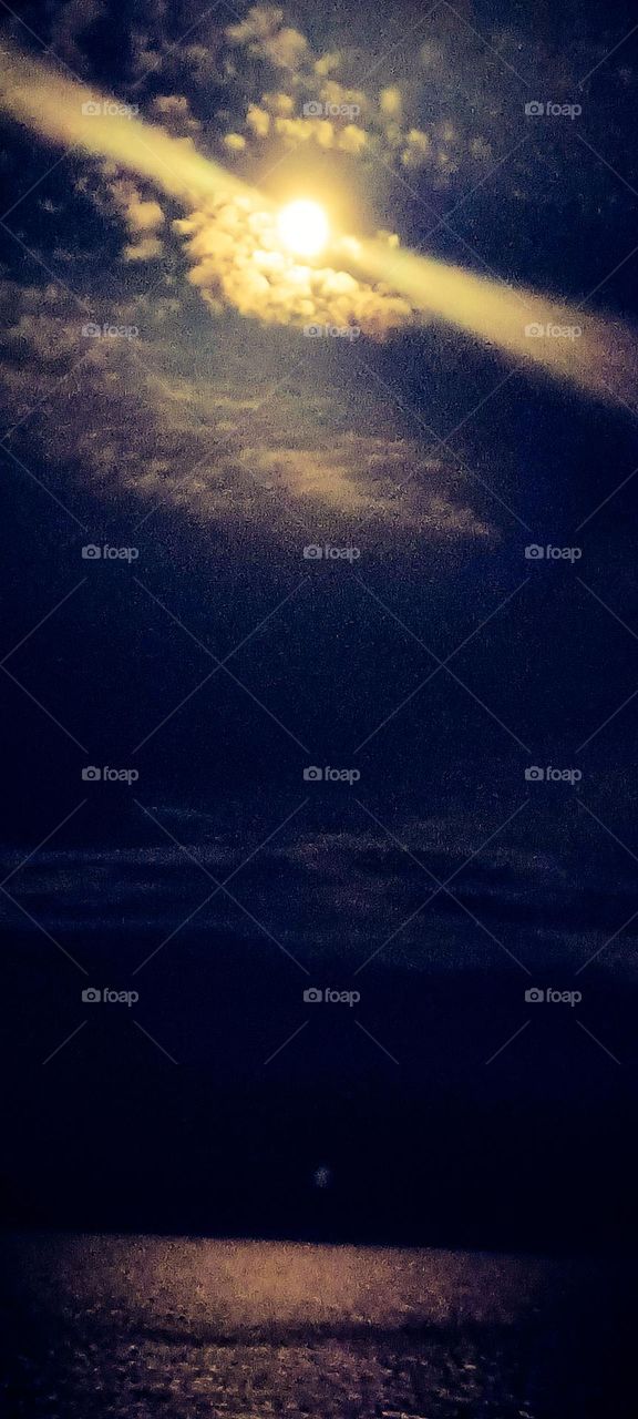 A view of the ocean in the dark with the clouds and the moon beams raining down 