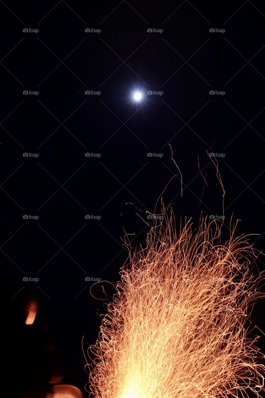 A blazing fire at night with a full moon above.