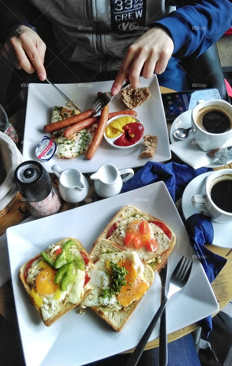 Top view of people having traditional english breakfast with sausages and fried eggs