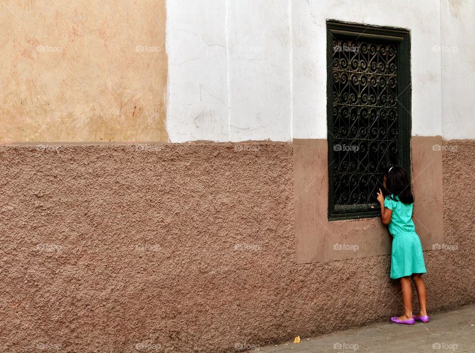 Little Moroccan girl dressed in green peeps through a window, spying through a window 