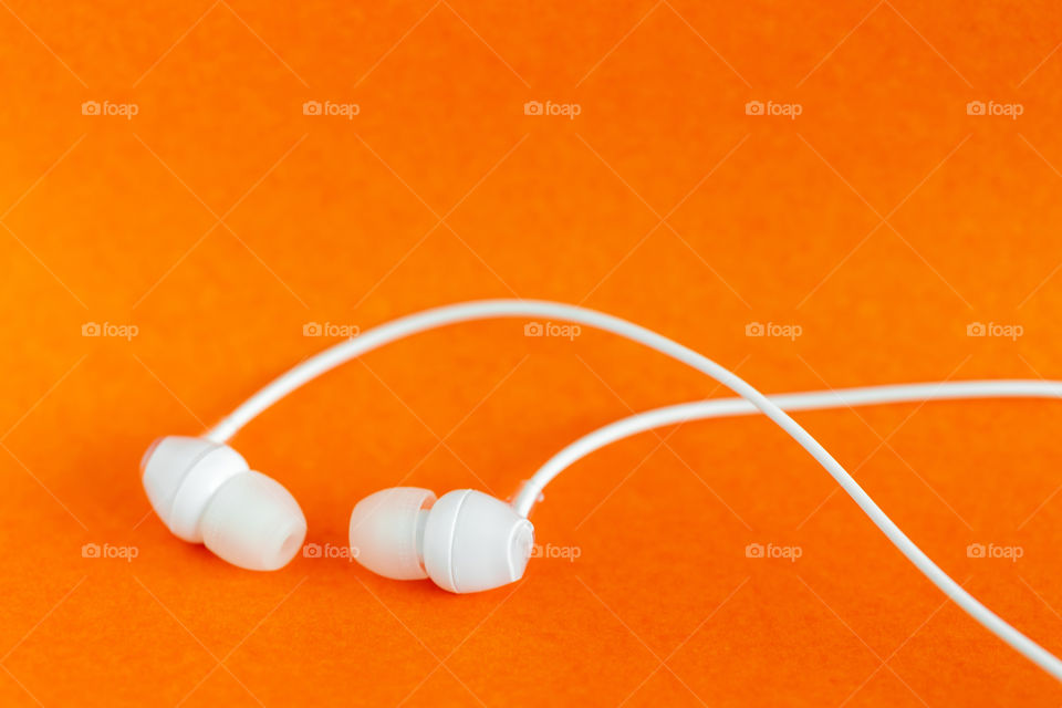 Earbuds on bright orange background. Minimalism concept with copy space.