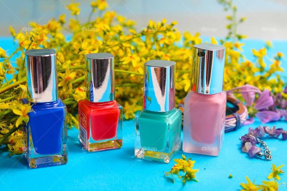 Nail poliches,  yellow flowers and jewelry on a blue background.  The dominance of rainbow colors