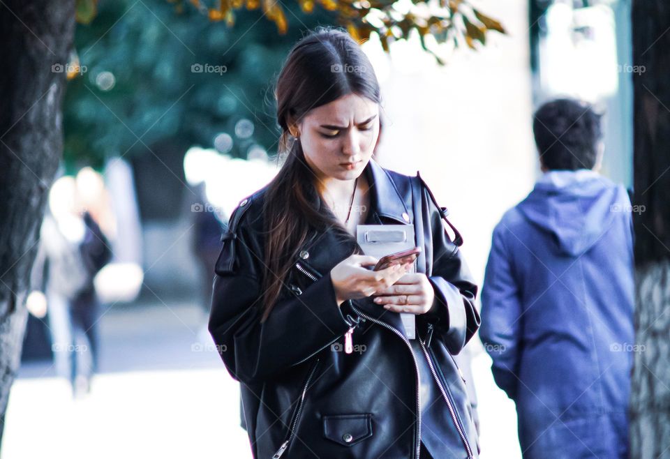 A cute young girl walks down the street and carefully writes something on her phone.