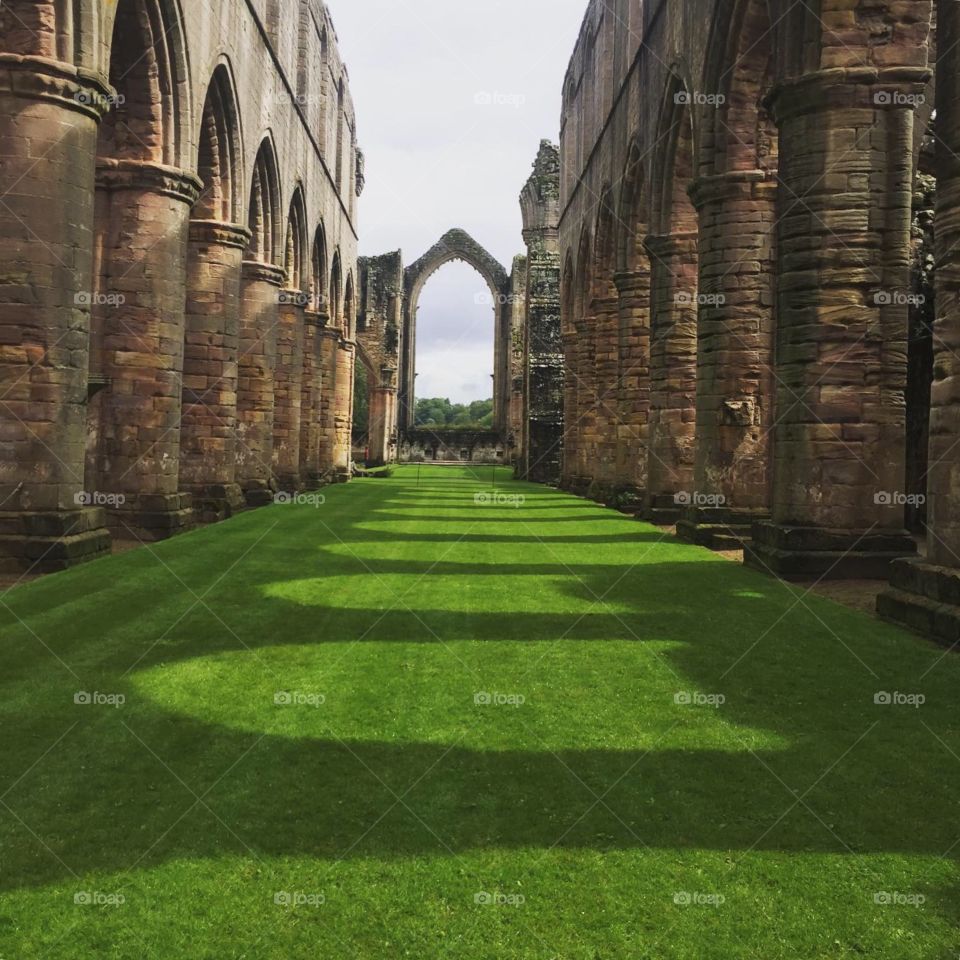 Central grass area of abbey ruins with cloisters on either side and a glass less window at the far end 