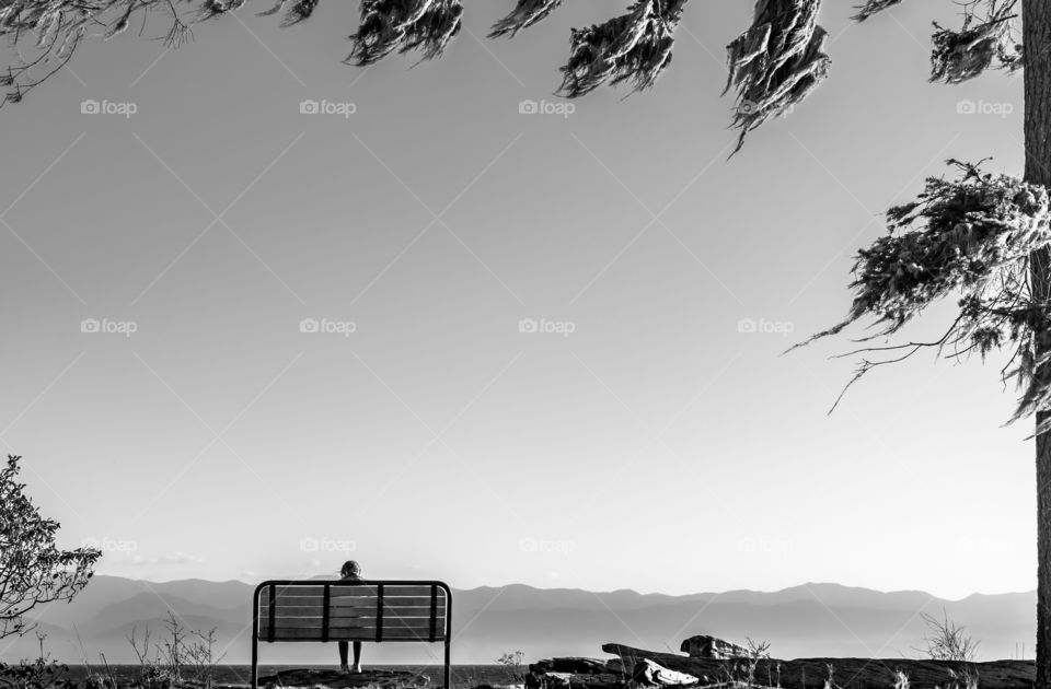 Lone person sitting on a bench in open space with mountains in the distance 