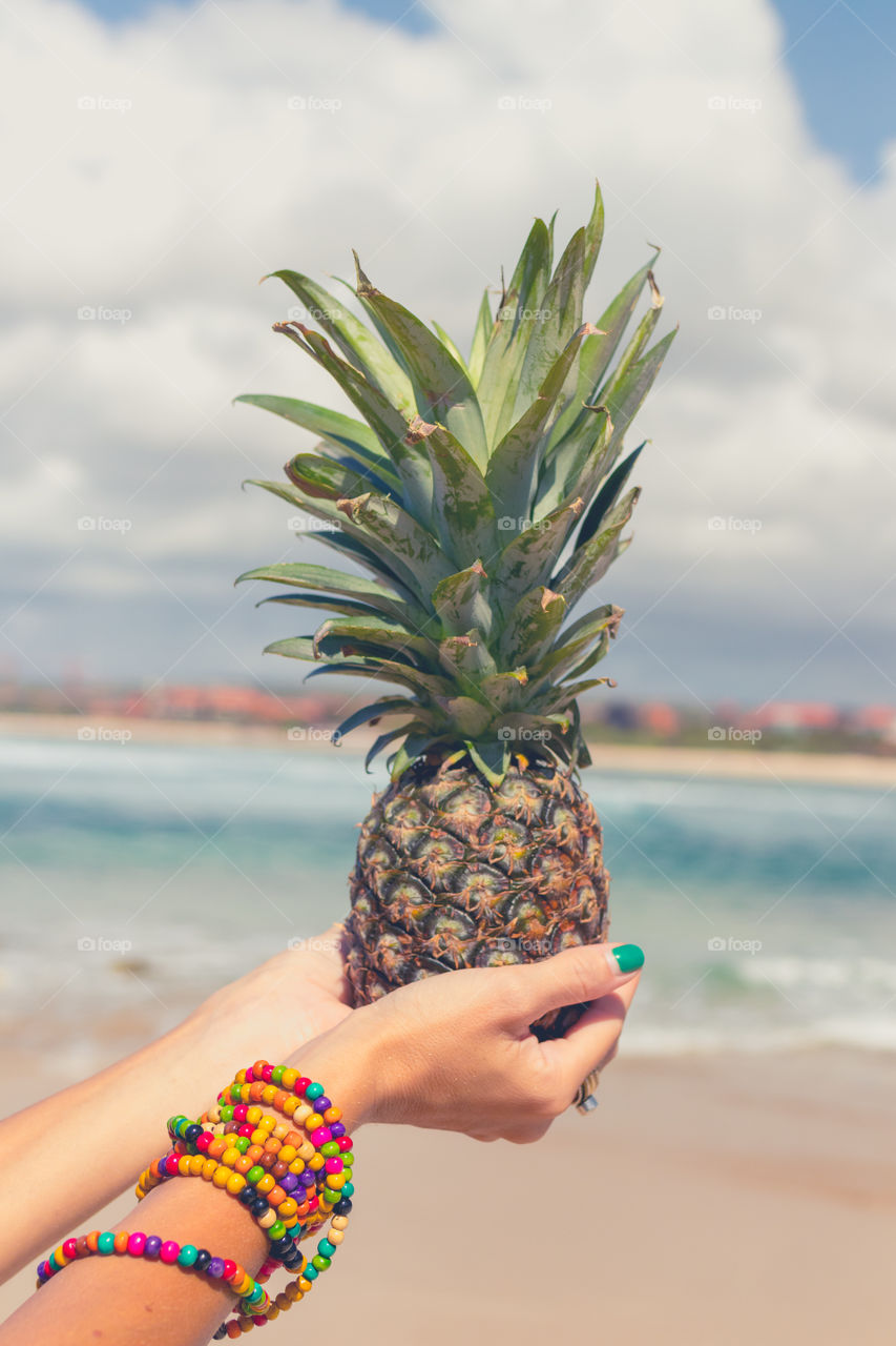 The girl is holding a pineapple. In the background is the Indian ocean. Bali island.