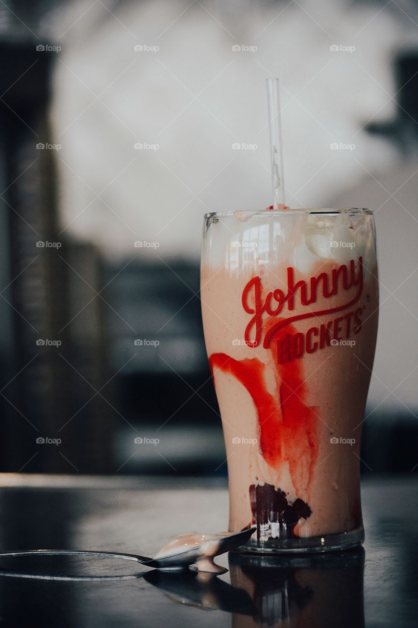 strawberry milkshake with whipped cream and strawberry sauce dripping down the side of the glass cup, with a milkshake spoon dripping messy. pink and glass vintage glass aesthetic diner straw