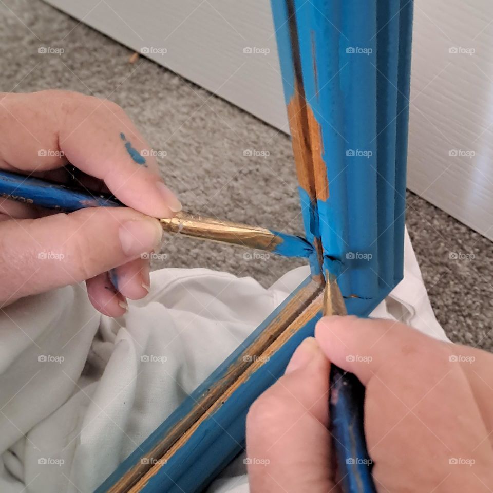 hand reflection in mirror being pained with small brush and blue paint. diy painting mirror frame