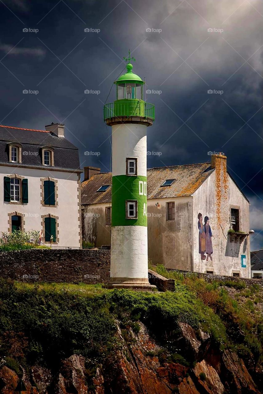 Close up on Doëlan white and green lighthouse and the houses standing behind on a dark grey cloudy day in Clohars-Carnoët