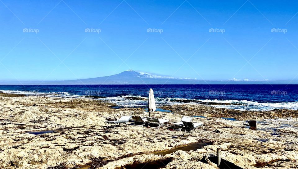 Sun loungechairs on the rocks by the sea overlooking the volcano 