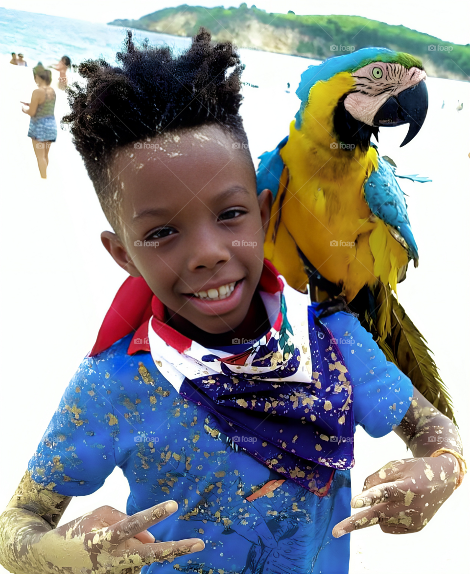 A young African boy, smiling brightly, stands on a sunny beach. The waves gently crash in the background. A colorful parrot perches on his shoulder, its vibrant feathers contrasting with the boy’s radiant expression.