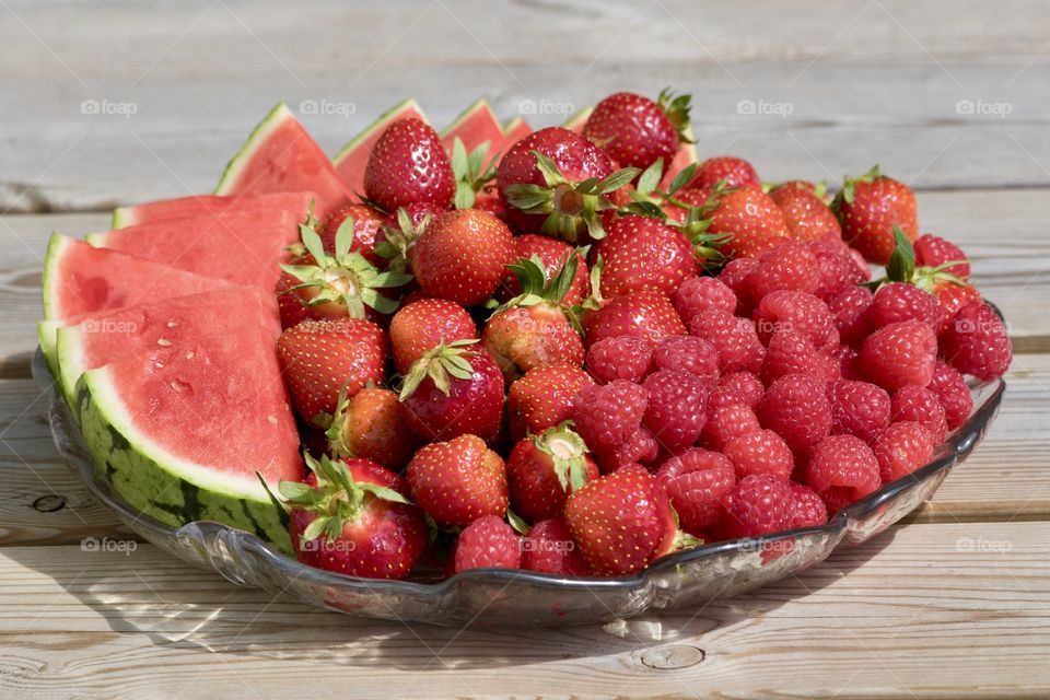 Enjoying fresh healthy strawberries raspberries watermelon on glass plate in June 