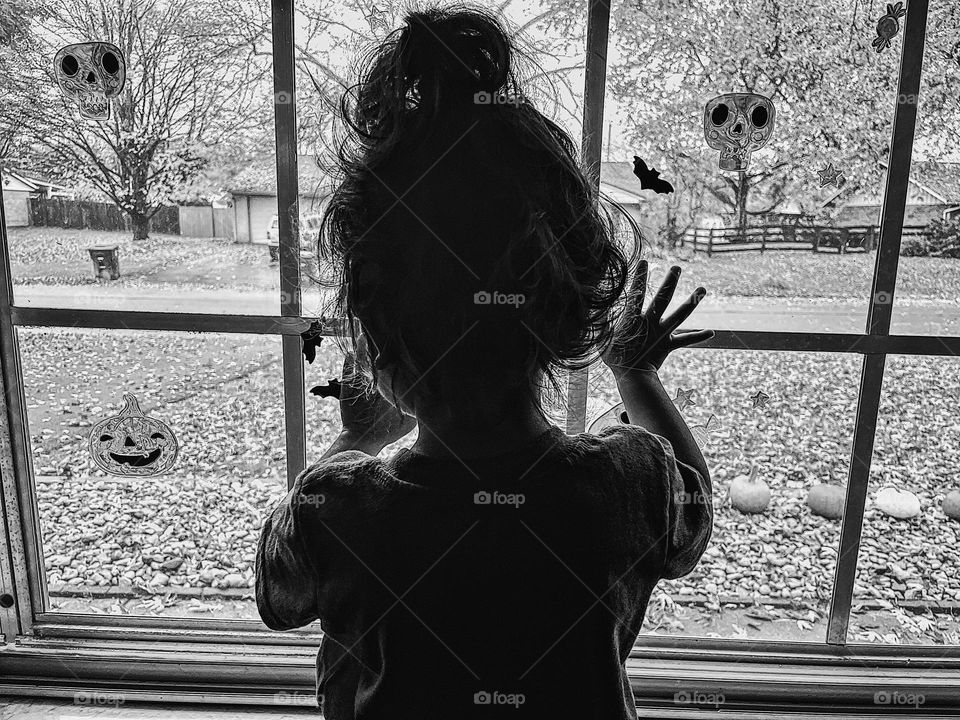 Toddler child helps decorate for Halloween, black and white Halloween decorating image, monochromatic child helping with decorating for Halloween, child looking out window 