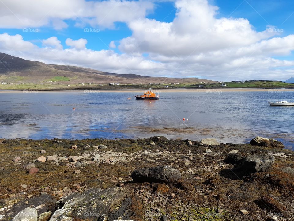 Irish shoreline with boats, seaweed and mountains, summer landscape