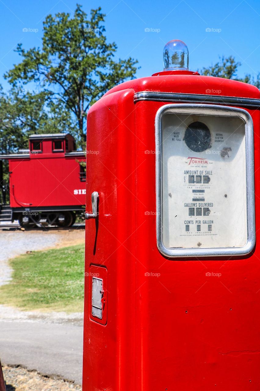 Vintage red gas pump with red train caboose in the background harkening to days gone by 