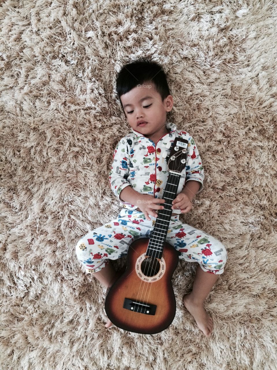 High angle view of a boy lying on carpet with guitar