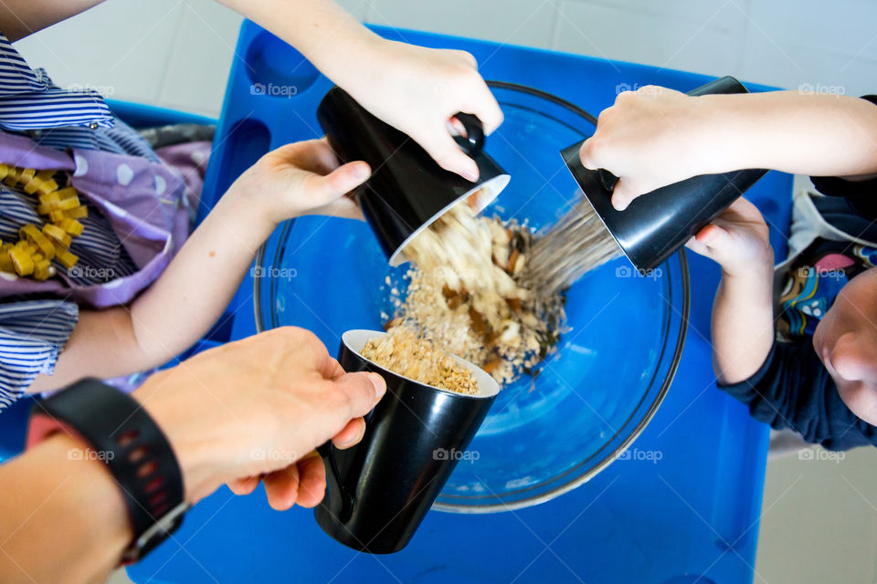 Making homemade gronola at home with my kids. Image of mom, daughter and son putting together ingredients for baking using cups.