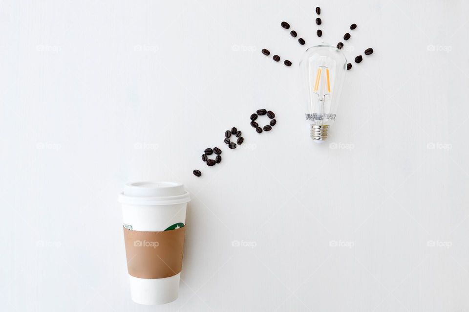 Minimalist image of a white disposable coffee cup with coffee beans in the shape of a thought bubble with lightbulb extending off of it 