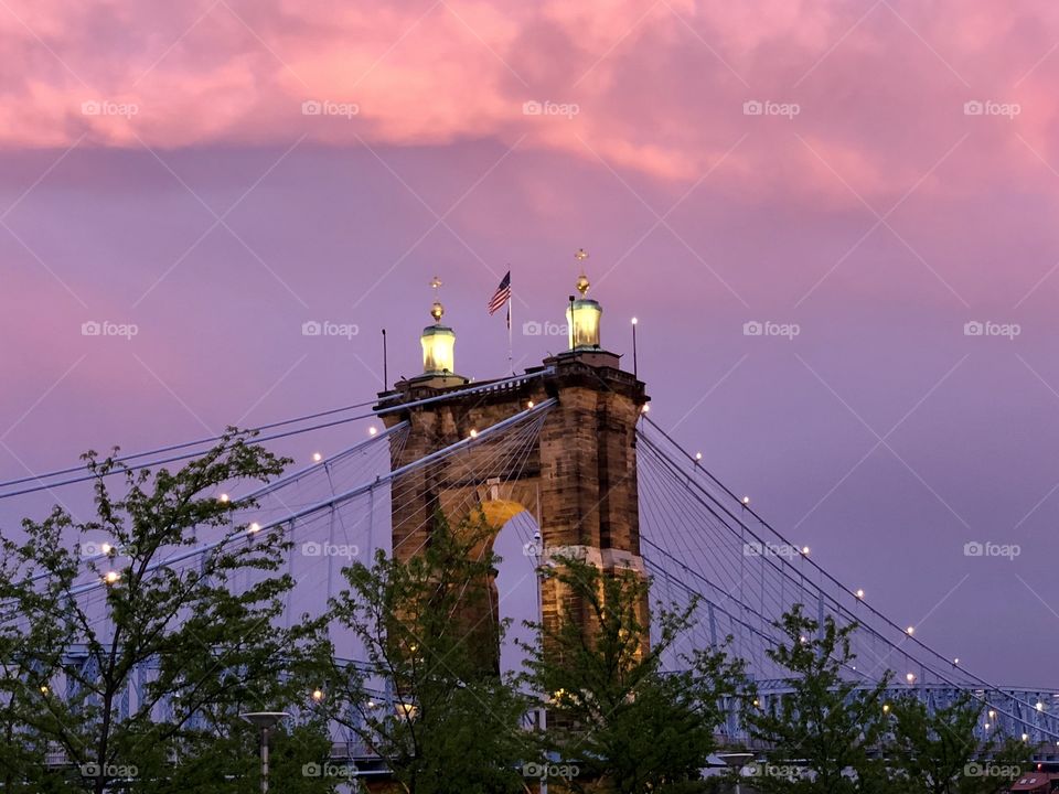 John A. Roebling suspension bridge at dusk in Cincinnati, OH. American flag flying at the top.