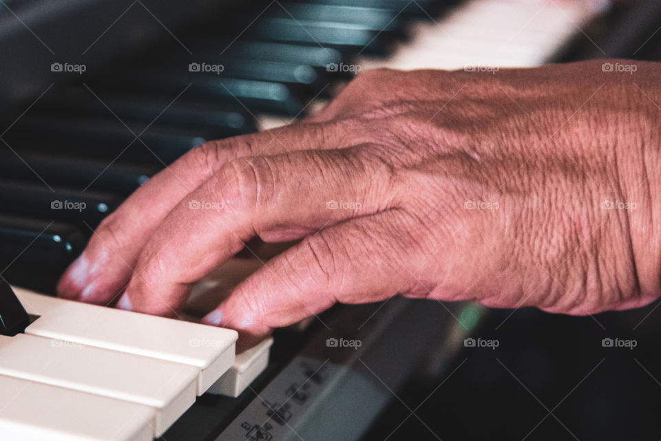 An old man’s hand on a keyboard’s key, playing music to calm his soul