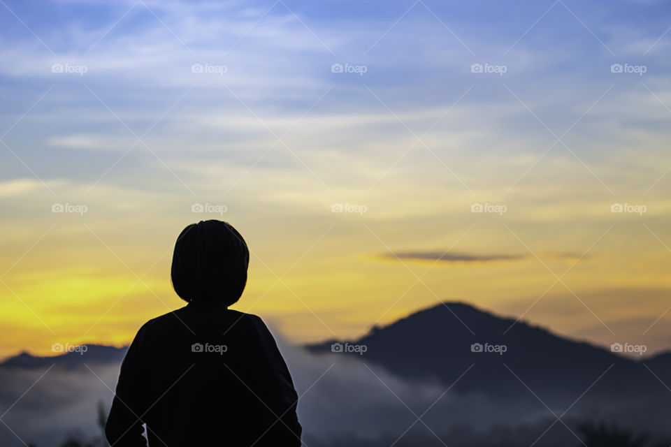 Blurry morning sun light behind the mountains with the shadow of a woman and The mist.