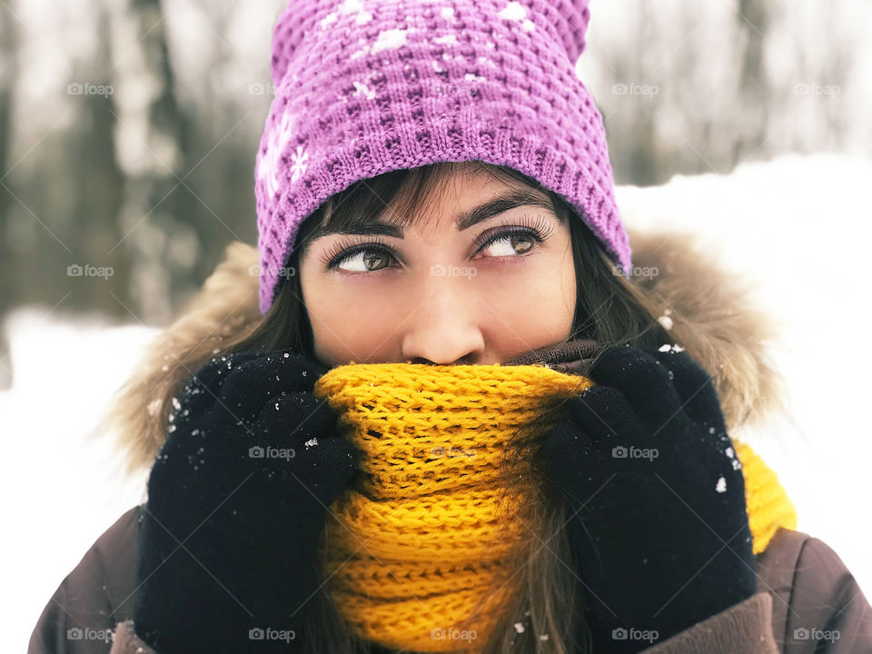 Portrait of a young woman wearing winter hat and scarf covered by fresh snow 