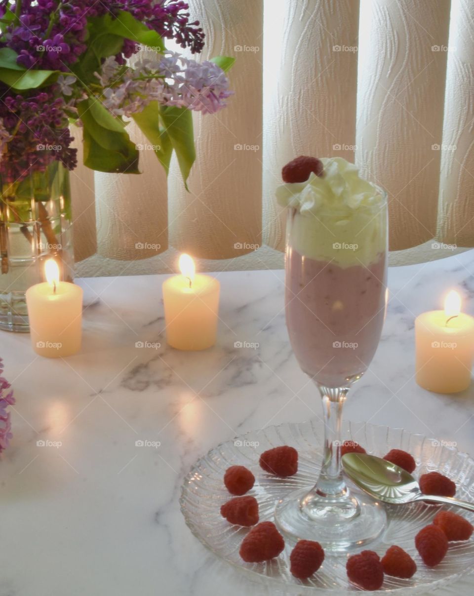 Summer treat, berry smoothie with whipped cream, raspberries, candles, and flowers in a vase