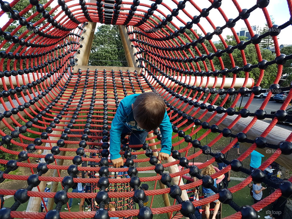 boy playing on playground climbing equipment, rope tunnel