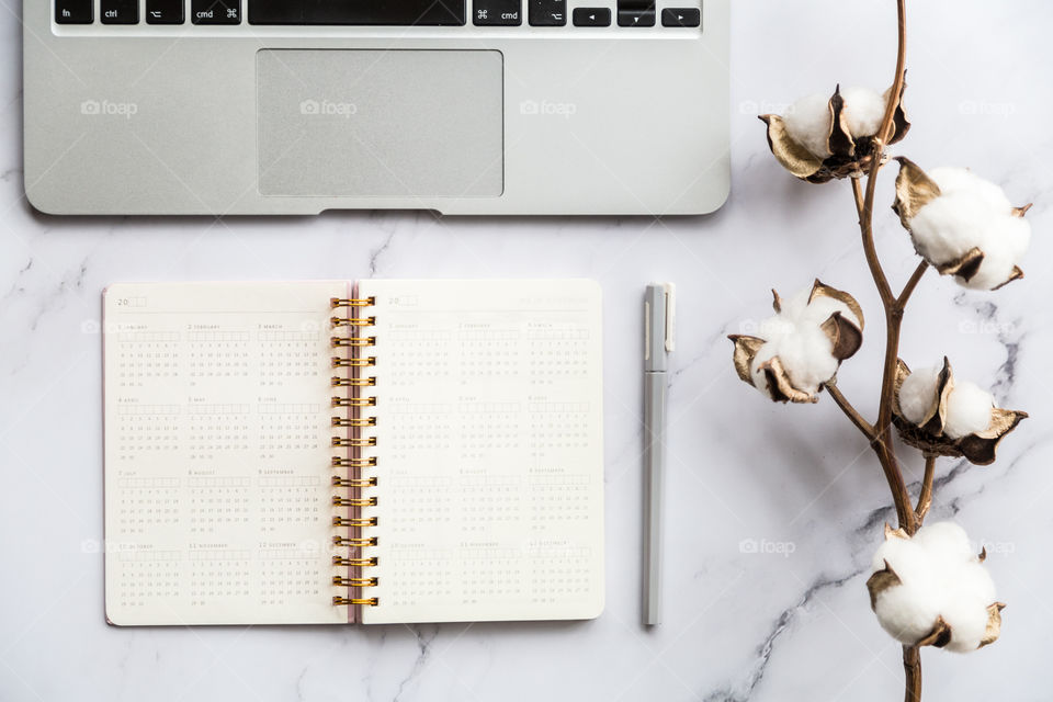 Desktop flatlay items: laptop, calendar, eyeglasses, candle, earrings, pen, cotton flowers lying on marble background 