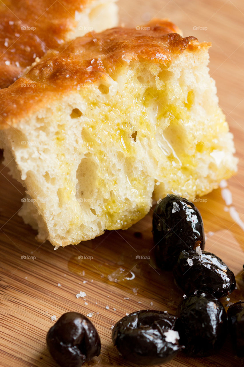 Focaccia bread with olives. Chunk of focaccia bread with olive and olive oil on a wooden board 