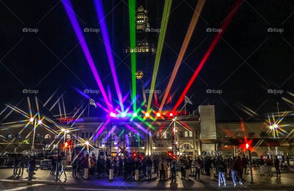San Francisco Pride 2023 laser light display of the pride flag colors illuminating the sky in front of the Ferry Building on the Embarcadero as people gather to celebrate