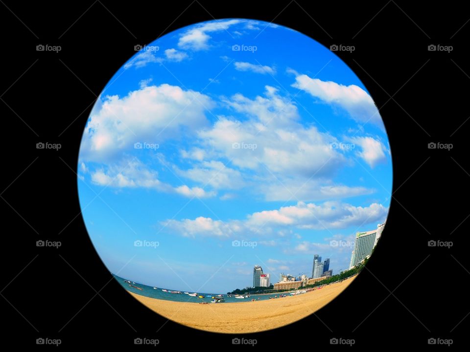 Beach, blue skies, clouds and buildings in fisheye view.