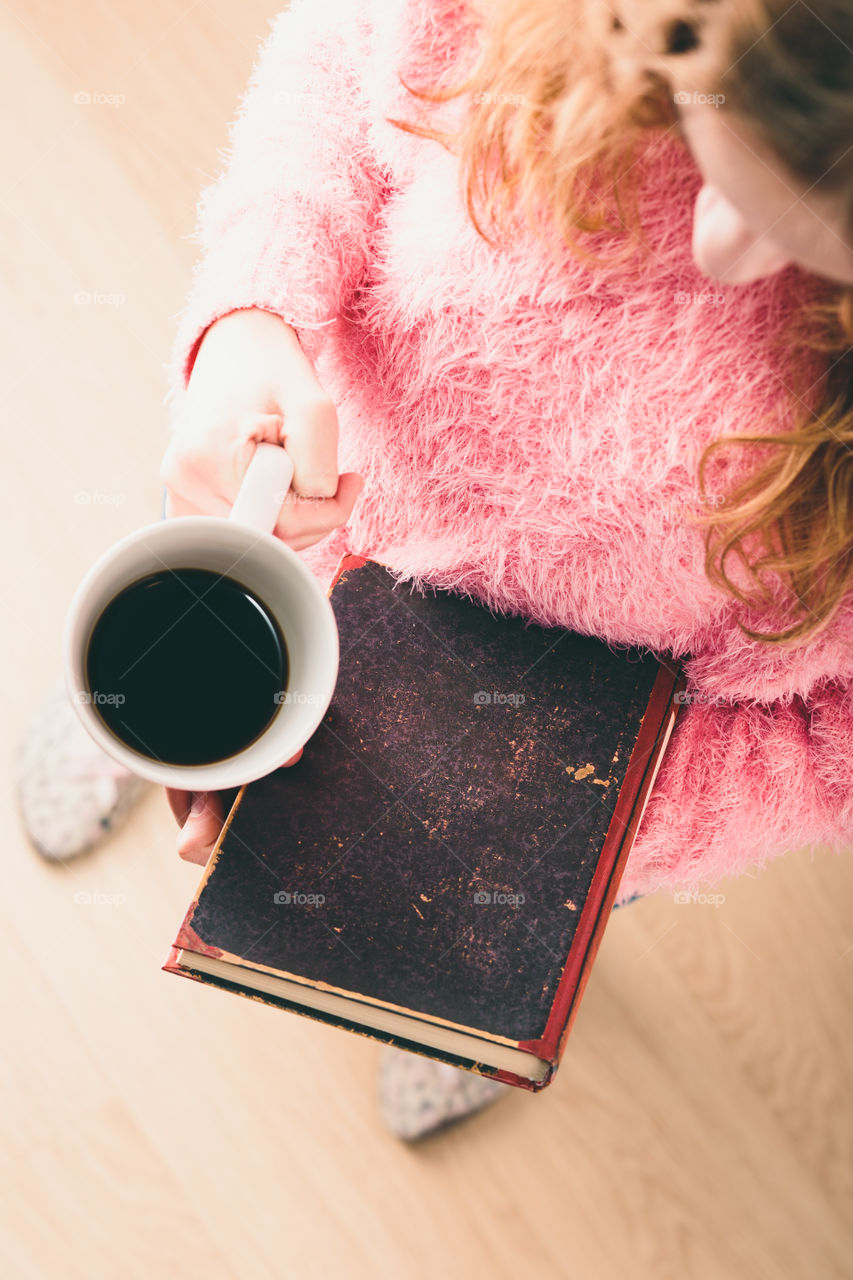 Enjoying the reading a book. Young girl holding book and cup of coffee going to relax with book. View from top