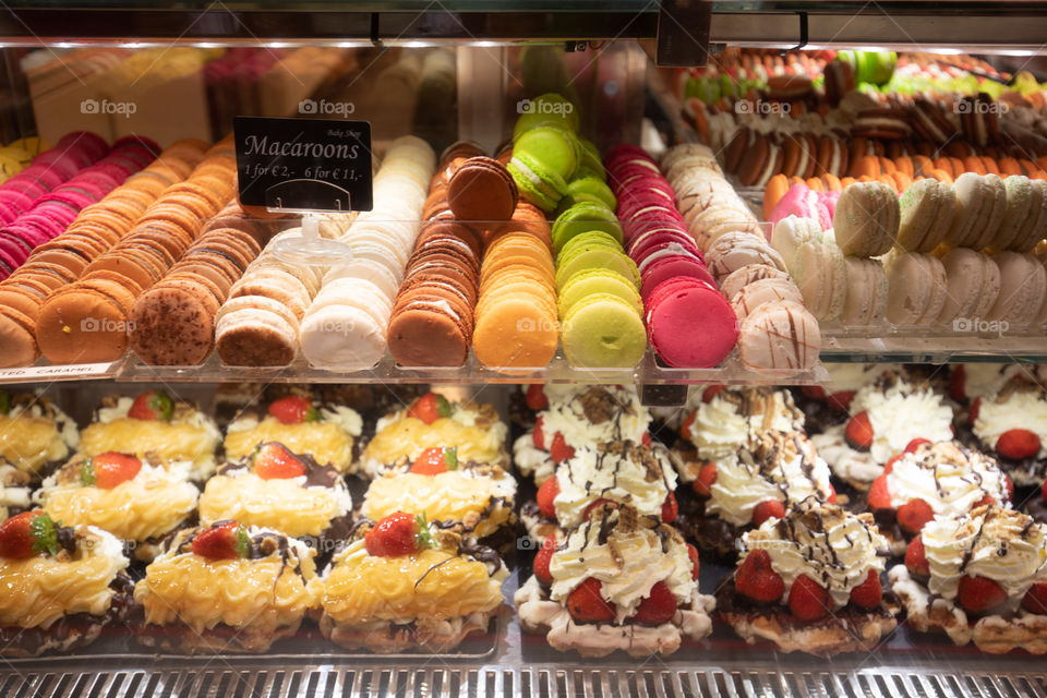 Colorful cup cakes, macarons, tarts, cakes, in a shop window. Candies, sweets and desserts at the store.