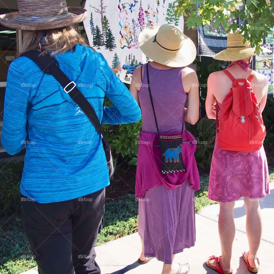 A group of ladies admiring a row of quilts hanging from a building at the Annual Sisters Quilt Show in Central Oregon in the summer. 