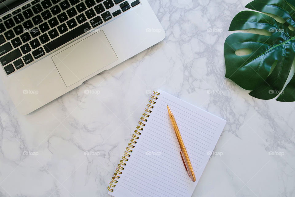 Modern desktop with marble, laptop, notebook and rose gold pen, monstera leaf; female entrepreneur workspace flat lay