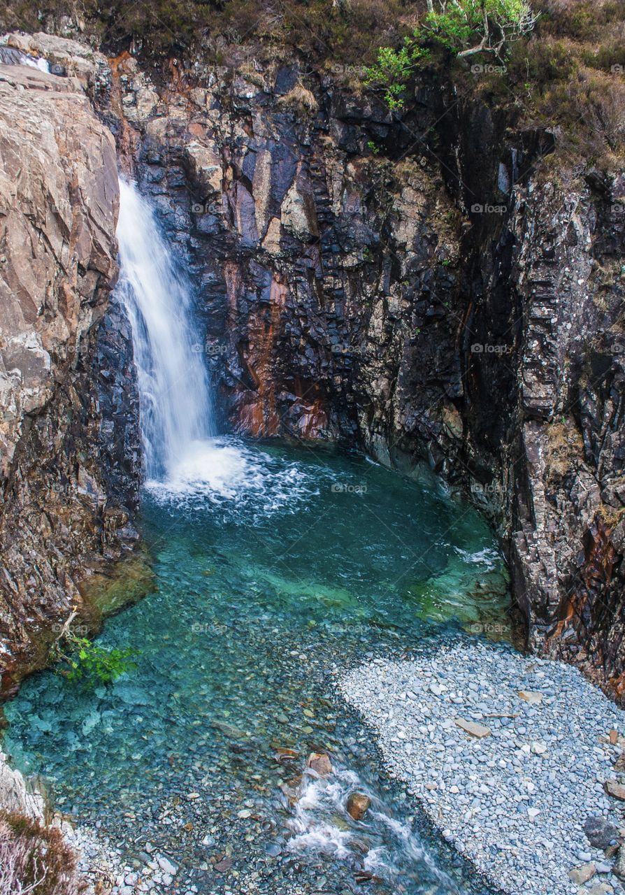 A waterfall tumbles from the rocks to form a clear, blue water pool below - Fairy Pools - Isle of Skye - Scotland 2013