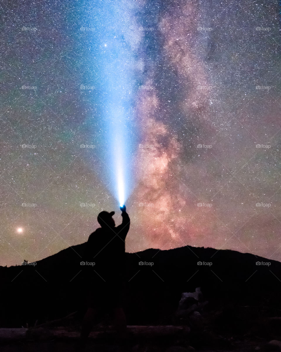 Silhouette of a man stargazing out in the wilderness, with the core of the Milky Way shining brightly in the night sky.