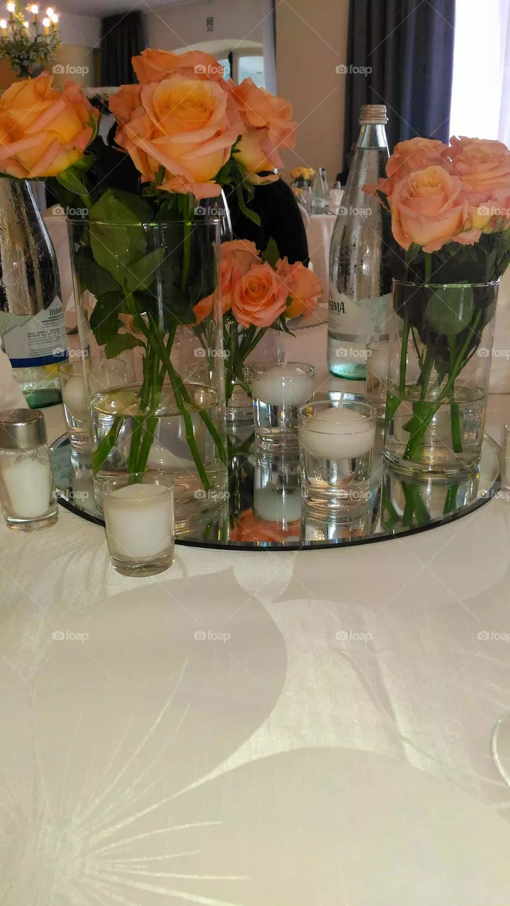 A wedding centrepiece with a bouquet of orange roses on a mirror tray surrounded by little white candles