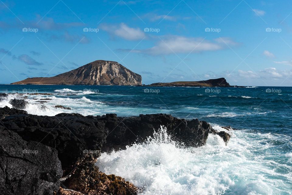 Islands of the coast of Ohau Hawaii with waves crashing against the black coral coastline
