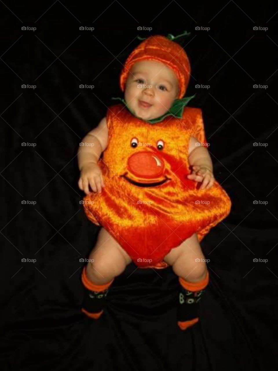 happy 7 month old baby laughing dressed in a cute Halloween , pumpkin costume 

isolated on black